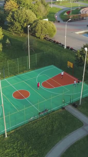 人々は緑の都市公園の裁判所でバスケットボールをしている 空からの眺め ドローンが飛び回っている 遠隔ショット バーティカルビデオ — ストック動画