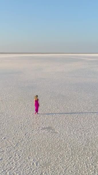 長い髪を持つ赤いドレスの若い白人女性だけが巨大な塩湖の白い表面を歩いています 空からの眺め バーティカルビデオ — ストック動画