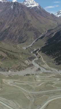 Yüksek dağlardaki kıvrımlı Yılan Yolu Geçidi. Drone ileri uçuyor, Kamera aşağı eğiliyor. Atış ayarlanıyor. Dikey Video