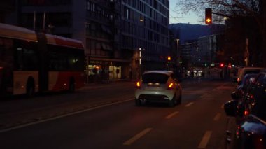 GENEVA, SWitzERLAND - 20 Şubat 2024: Trolleybus and People at Busy Street at Evening Twilight. Mavi Saat