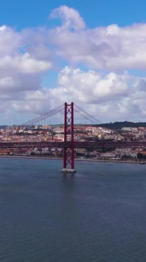 Ponte 25 de Abril Askı Köprüsü ve Lisbon Skyline. 25 Nisan Köprüsü. Mavi Gök ve Kümülüs Pofuduk Bulutları. Portekiz. Hava görüntüsü. Drone ileri ve yukarı doğru uçuyor. Orta boy shot. Dikey Video