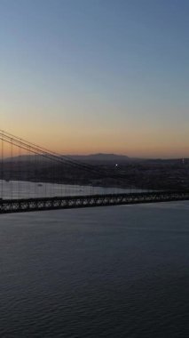 Tagus Nehri üzerindeki 25 de Abril Askı Köprüsü, Sunset. 25 Nisan Köprüsü. Portekiz. Hava görüntüsü. Geniş açı. Drone yukarı ve geri hareket ediyor. Dikey Video