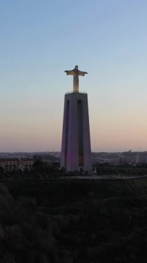 ALMADA, PORTUGAL - 2 Mart 2023: Cristo Rei Heykeli ve Almada Şehri, Portekiz Sunset. Kral heykeli İsa. Hava görüntüsü. Altın Saat. Yörüngede. Dikey Video