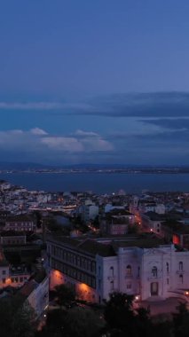 Akşam Alacakaranlığı 'nda Lizbon Eski Şehir Skyline ve Tagus Nehri' ni aydınlattı. Mavi Saat. Portekiz. Hava görüntüsü. Drone ileri ve yukarı doğru uçuyor. Dikey Video