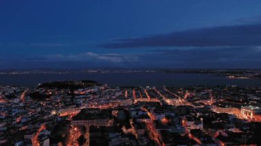Geceleri Lizbon Eski Şehir Skyline ve Tagus Nehri 'ni aydınlatırdı. Mavi Saat. Portekiz. Hava görüntüsü. Drone İleri Uçuyor