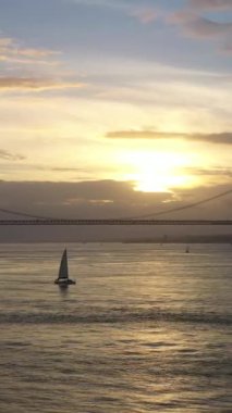 Sunset ve Yelkenli Yat 'ta 25 Nisan Askı Köprüsü. Ponte 25 de Abril ve Tagus Nehri. Portekiz. Hava görüntüsü. Altın Saat. Yörüngede. Orta boy shot. Dikey Video