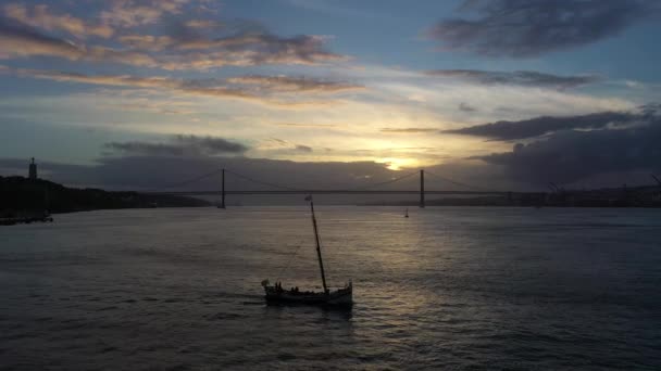4月25日日落时的吊桥和帆船驶过的轮廓 Ponte Abril和Tagus River 葡萄牙 空中静态射击 黄金时间 — 图库视频影像