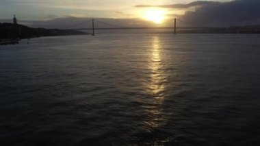 Sunset 'te 25 Nisan Askı Köprüsü. Ponte 25 de Abril ve Tagus Nehri. Portekiz. Hava görüntüsü. Altın Saat. İnsansız hava aracı ileri, yana doğru hareket ediyor. Görüntü Görüntüsü