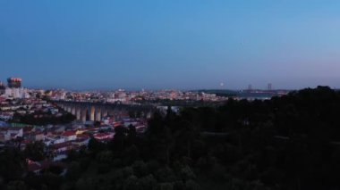 Lisbon Skyline ve Akşam Alacakaranlığı 'ndaki Monsanto Ormanı Parkı. Aguas Livres Aqueduct. Mavi Saat. Portekiz. Hava görüntüsü. Drone ileri ve yukarı hareket ediyor. Görüntü Görüntüsü