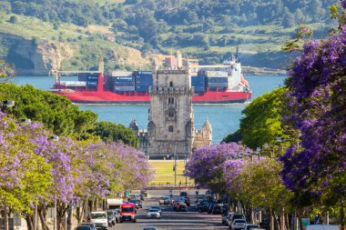 LISBON, PORTUGAL - 25 Mayıs 2024: Belem Tower, Jacaranda Çiçek açan Mor Ağaçlar ve Kargo Konteynır Gemisi.