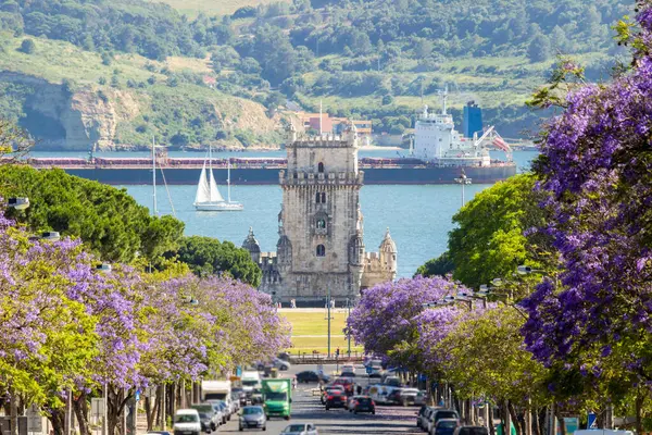 Belem Kulesi, Jacaranda Çiçek açan Mor Mavi Ağaçlar, Büyük Mavna ve Güneşli Gün Yelkenli Teknesi. Lizbon, Portekiz.