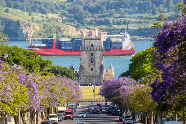 LISBON, PORTUGAL - 25 Mayıs 2024: Belem Tower, Jacaranda Çiçek açan Mor Ağaçlar ve Kargo Konteynır Gemisi.