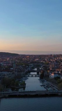 ZURICH, SWitzERLAND - 28 Nisan 2024: Zürih Eski Şehir Skyline ve Sunset Limmat River. Altın Saat. İsviçre. Hava görüntüsü. Drone ileri ve yukarı hareket ediyor. Dikey Video