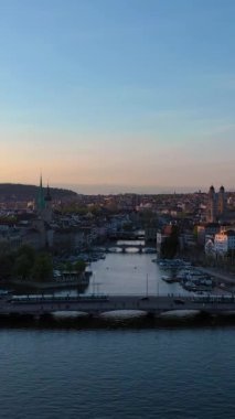 ZURICH, SWitzERLAND - 28 Nisan 2024: Zürih Eski Şehir Skyline ve Sunset Limmat River. Altın Saat. İsviçre. Hava görüntüsü. Drone ileri geri hareket ediyor. Dikey Video