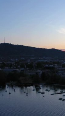 Zürih Şehri, Sunset, Uetliberg Dağı ve Zürih Gölü 'ndeki tekneler. Şehrin batı yakası, Enge Bölgesi. Altın Saat. İsviçre. Hava görüntüsü. İnsansız hava aracı yan yana hareket ediyor. Dikey Video
