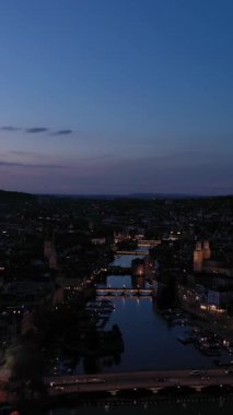 Geceleri Zürih Şehri Eski Şehir ve Limmat Nehri 'ni aydınlatırdı. Mavi Saat. Temiz Gökyüzü. İsviçre. Hava görüntüsü. Drone geriye doğru hareket ediyor. Dikey Video