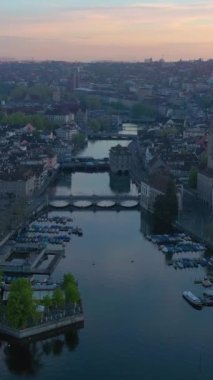 Zürih Şehri Eski Şehir ve Gündoğumunda Limmat Nehri. Altın Saat. İsviçre. Hava görüntüsü. İnsansız hava aracı aşağıya doğru hareket ediyor, yukarı doğru. Turna Vuruşu. Dikey Video