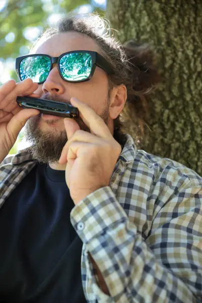 At kuyruklu adam güneş gözlüğü takıyor mızıkayla müzik çalıyor, Mouth Organ. Güneşli yaz gününde Green Park 'ta dikilmek. Orta boy Yakın Çekim