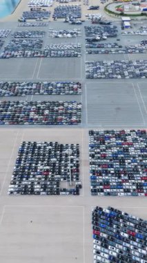 Port 'taki Büyük Boş Otoparktaki Yeni Arabalar Dağıtıma Hazır. İhracat ve İthalat için Liman Araç Deposu. Otomotiv endüstrisi. Hava Yüksek Açı Görünümü. Yanlamasına hareket ediyor. Dikey Video