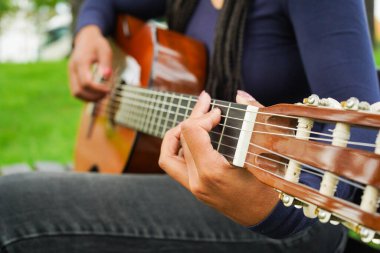 Kahverengi derili kadın ve Yeşil Park 'ta oturan ve gitar çalan uzun siyah saçlı kadın. Orta Çekim