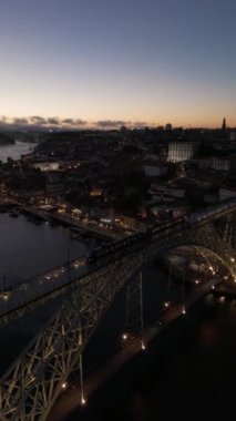Aydınlatılmış Porto Şehri, Douro Nehri ve Dom Luis Köprüsü ile Akşam Alacakaranlığı Tramvayı. Mavi Saat. Portekiz. Hava Aracı Atışı. İleri, aşağı doğru hareket edin. Dikey Video