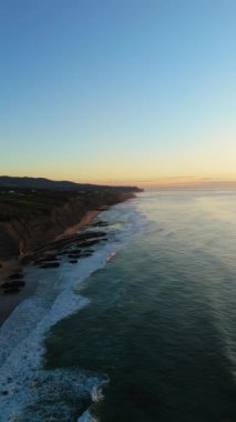 Low Tide sırasında Sunset 'teki Magoito Sahili ve Kayalıkları. Atlantik Okyanusu, Portekiz. Altın Saat. Hava görüntüsü. Geri çekiliyorum. Dikey Video