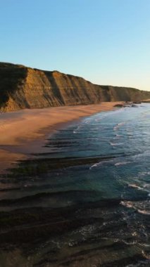 Low Tide sırasında Sunset 'teki Magoito Sahili ve Kayalıkları. Atlantik Okyanusu, Portekiz. Altın Saat. Hava görüntüsü. Kayaların üzerinden ilerliyoruz. Dikey Video