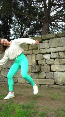 Beyaz ceketli, dışarıda dans eden genç ve güzel bir kadın. Tam doz. Dikey Video