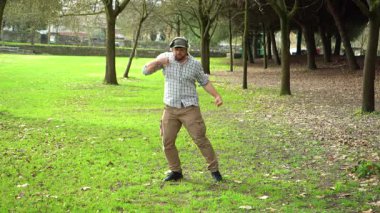 Green Park 'ta dans eden kulaklıklı orta yaşlı amatör dansçı. Hızlı Enerji Hareketleri. Tam Vuruş