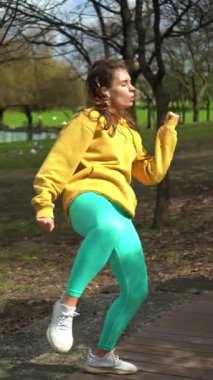 Sarı kapüşonlu güzel kadın dışarıda dans eden zumba fitness dansı yapıyor. Tam doz. Dikey Video