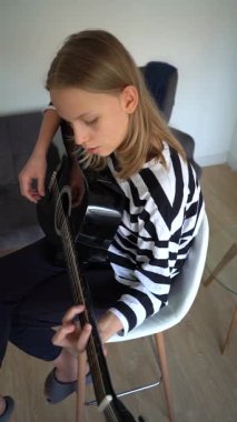 13 yaşında, evde gitar çalan genç bir kız. Dikey Video.