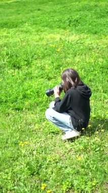 11 yaşındaki beyaz kız yeşil parktaki fotoğraf makinesiyle fotoğraf çekiyor. Dikey video