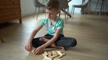 7 yaşında bir çocuk yerde küp oynuyor, kule inşa ediyor.