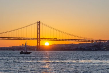 25 Nisan Askı Köprüsü, Yelkenli ve Tagus Nehri, Sunset. Lizbon, Portekiz. Cacilhas 'tan Görünüm