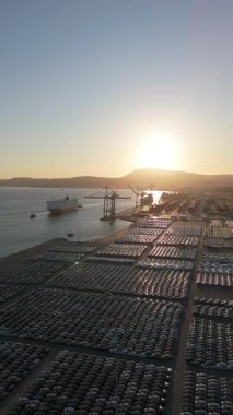Ro-Ro Kargo Gemisi Geliş ve Yeni Arabalar Port 'taki Sunset' te Büyük Tam Otopark Alanında. Araba Deposu. Okyanus ve Dağlar. Setubal, Portekiz. Hava görüntüsü. Geri çekiliyorum. Dikey Video