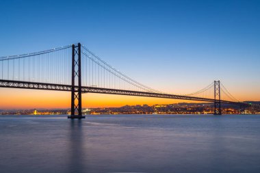 Alacakaranlık Gecesi 'nde Tagus Nehri üzerindeki Ponte 25 de Abril Askı Köprüsü. 25 Nisan Köprüsü. Portekiz. Mavi Saat