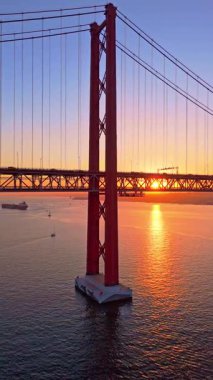 Tagus Nehri üzerindeki 25 de Abril Askı Köprüsü, Sunset. 25 Nisan Köprüsü. Portekiz. Hava görüntüsü. Sun, İnşaat 'tan gizlice bakıyor. Altın Saat. Dikey Video