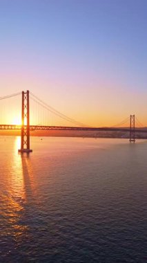 Tagus Nehri üzerindeki 25 de Abril Askı Köprüsü, Sunset. 25 Nisan Köprüsü. Portekiz. Hava görüntüsü. Geniş açı. Drone ileri gidiyor. Altın Saat. Dikey Video