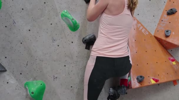 ボルダリングジムで壁に登る女性 女性登山訓練は ボルダリングクライミングの壁にかかっている アクティブライフスタイルと極端なスポーツコンセプト — ストック動画