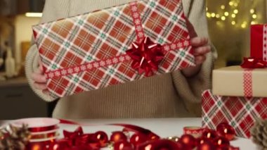 Sıcak süveter giymiş bir kadın hediye kutusunu hediye kağıdına sarmış, şenlikli kurdeleyle. Kış tatili hediyesi. Noel ve Mutlu Yıllar Kutlaması