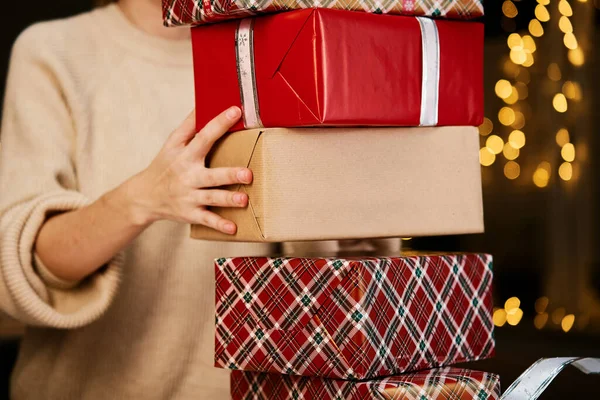 Woman prepares gifts for friends and relatives on Christmas eve. Woman holds pile of presents in gift boxes wrapping in craft paper