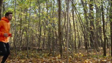 Sonbahar parkında koşan turuncu giysili bir adam. Erkek koşucu ormanda koşuyor. Sonbahar günü açık havada aktif spor egzersizleri. Sağlıklı yaşam tarzı