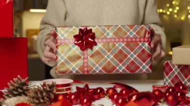 Sıcak süveter giymiş bir kadın hediye kutusunu hediye kağıdına sarmış, şenlikli kurdeleyle. Kış tatili hediyesi. Noel ve Mutlu Yıllar Kutlaması