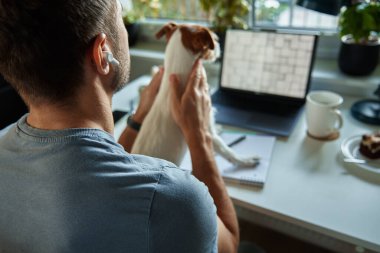 Evde köpekle çalışan Freelancer. Laptop kullanan ve not defterine yazı yazan kadın evdeki masada oturuyor..