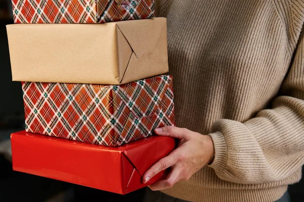 Woman prepares gifts for friends and relatives on Christmas eve. Woman holds pile of presents in gift boxes wrapping in craft paper