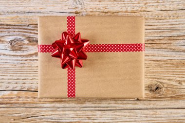 Şenlikli hediye kutusunun üstünde el sanatları kağıdına sarılmış, şenlikli kurdeleler ve fiyonklarla. Ahşap arka planda Noel tatili hediyesi