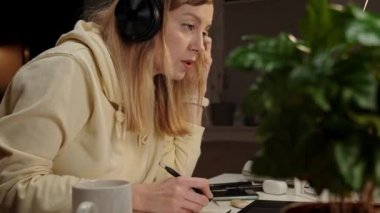 Kulaklık takan bir kadın karanlık odada oturuyor ve dizüstü bilgisayar kullanıyor. Ofisten geç saatlere kadar çalışıyorum. Kadın serbest çalışan, geceleri merkez ofiste çalışır, dizüstü bilgisayar kullanır.