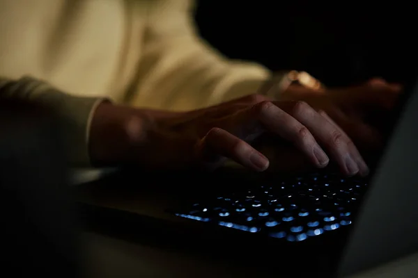 Close up shot of anonymous woman typing on laptop keyboard at night. Online communication and working after hours concept