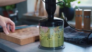 Female chopping avocado in blender. Woman preparing healthy breakfast at morning. Vegan food