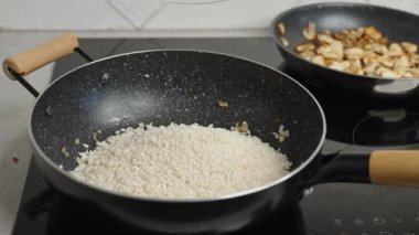 Process of cooking risotto. Cook adds arborio rice in frying pan, close up. Italian cuisine dish